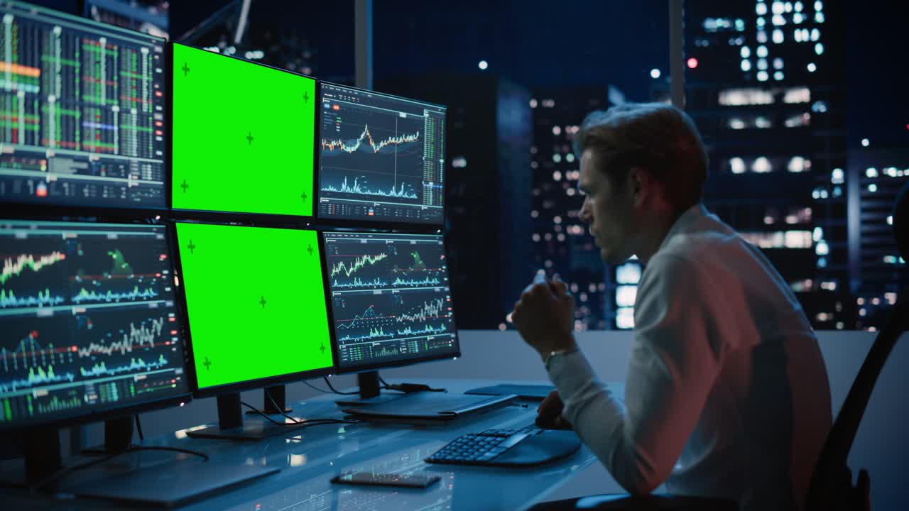 Financial Analyst Working on Computer with Multi-Monitor Workstation with Green Screen Chroma Key Mock Up Template and Real-Time Stock Charts. Businessman Works in Investment Bank in the Evening.