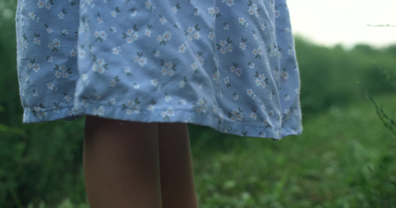 En piges blomstrede kjole flagrer blødt i vinden, hvilket understreger bevægelse og lys. Billedet føles let og filmisk.
