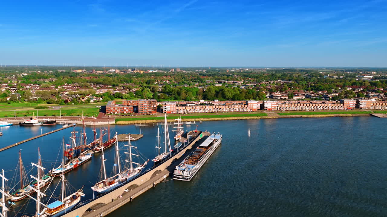 Boats with sails down standing at the berth in the port of Lelystad, the Netherlands. Approaching the lakefront of the city with lush greenery.