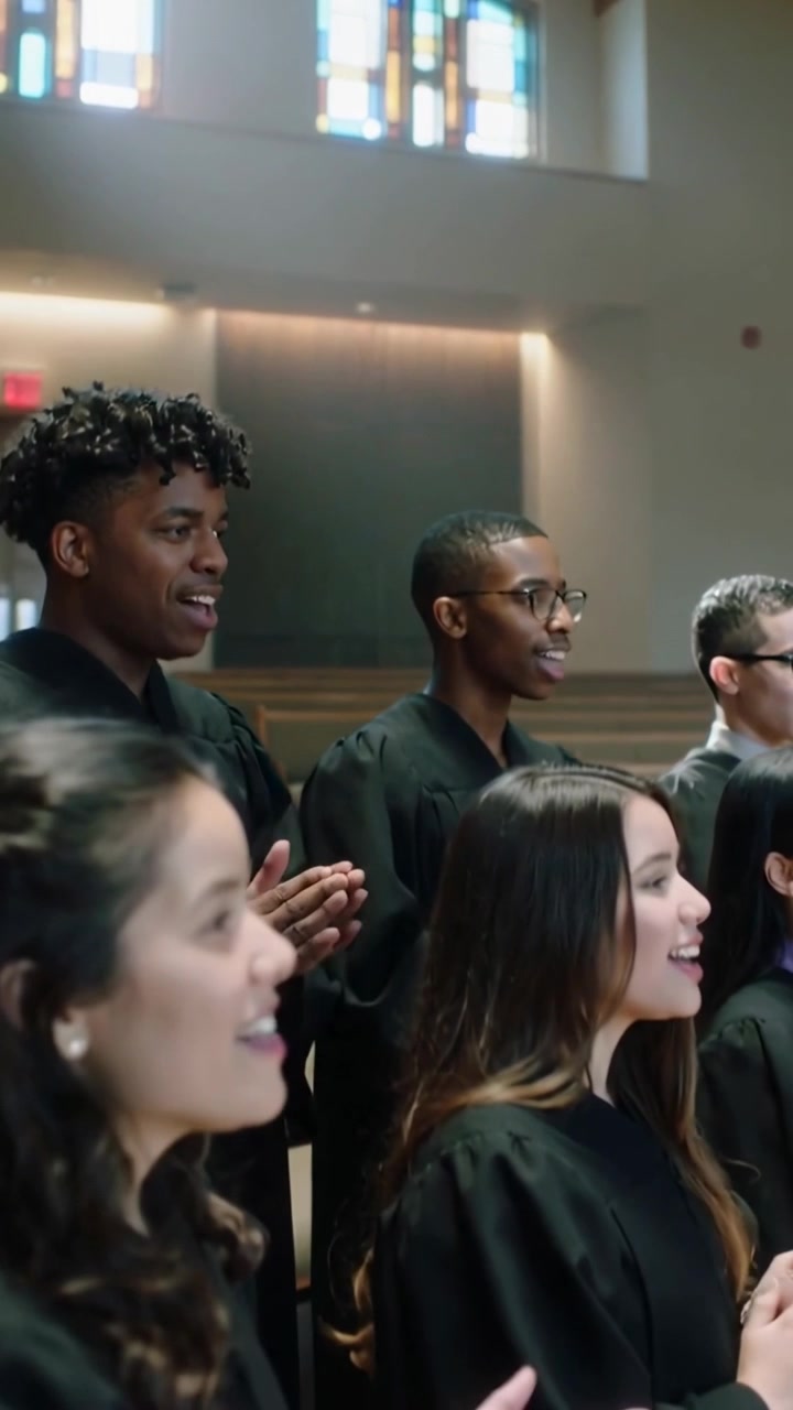 Video verticale: Membri del coro in prima fila che cantano, rispondendo all'attacco iniziale, applaudendo con le vesti liturgiche.