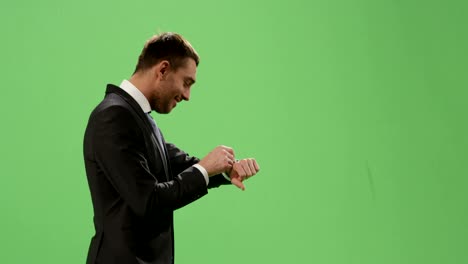 businessman in a suit is using a smartwatch while walking on a mock-up green screen in the background.