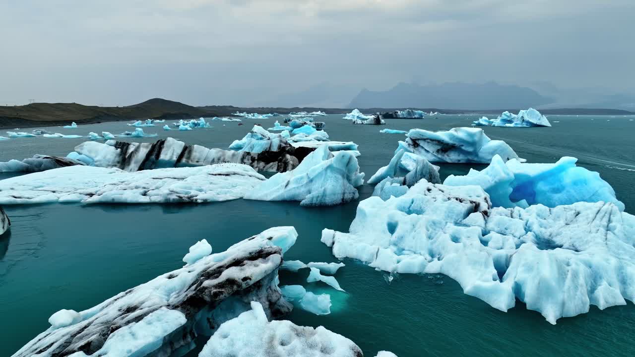 Wide drone view of scattered blue icebergs drifting across Iceland’s ...