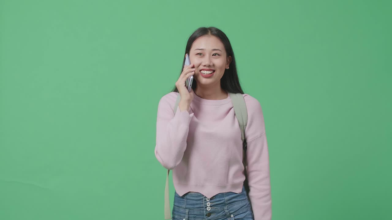 행복한 아시아 여성 학생이 녹색 스크린 스튜디오에서 는 동안 휴대 전화로 이야기합니다.