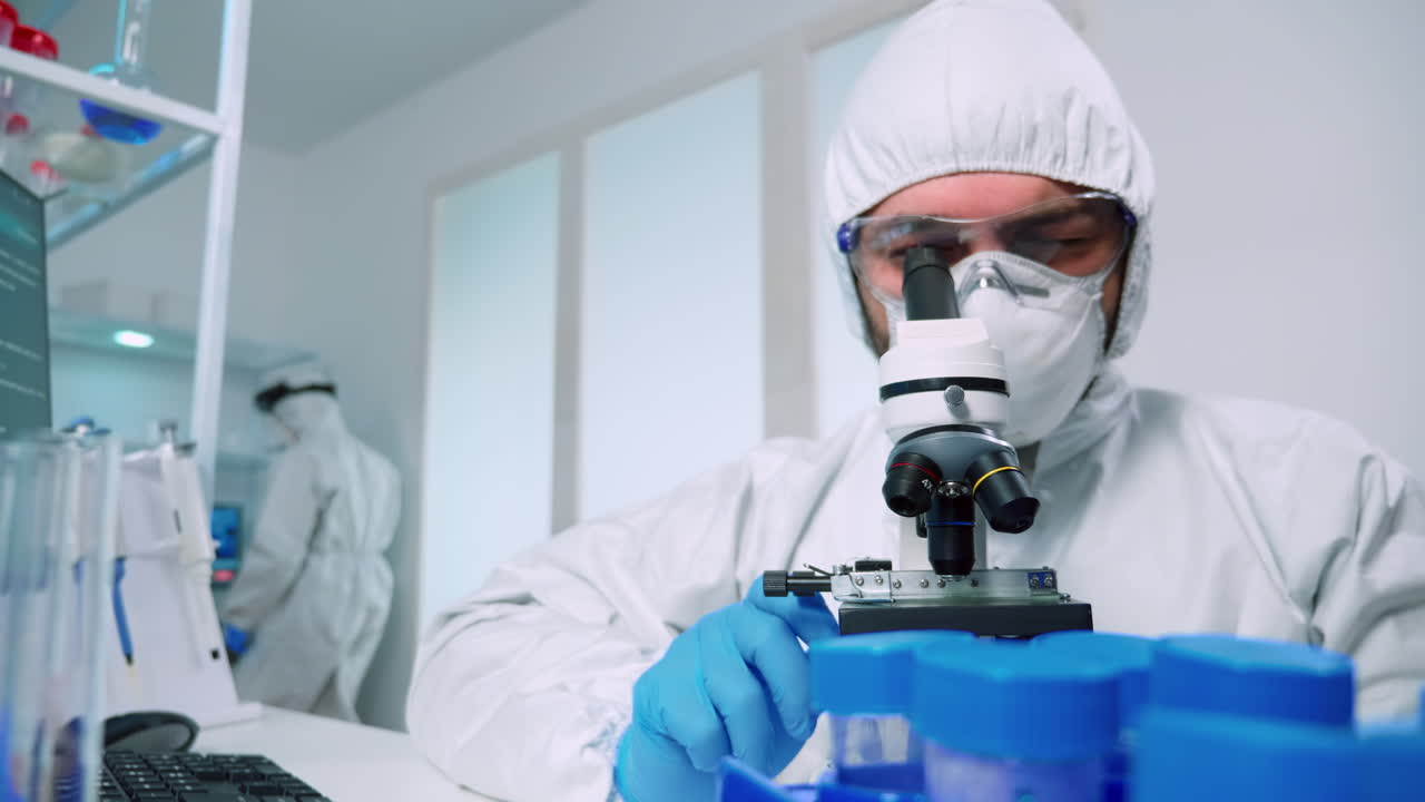 científico en traje de ppe realizando un experimento usando un microscopio