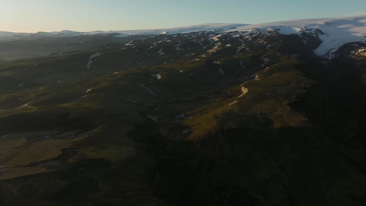 거대한 아이슬란드 고지대의 드론 촬영, 눈 인 산, 거친 지형, 그리고 풍경에 그림자를 던지는 부드러운 저녁 빛