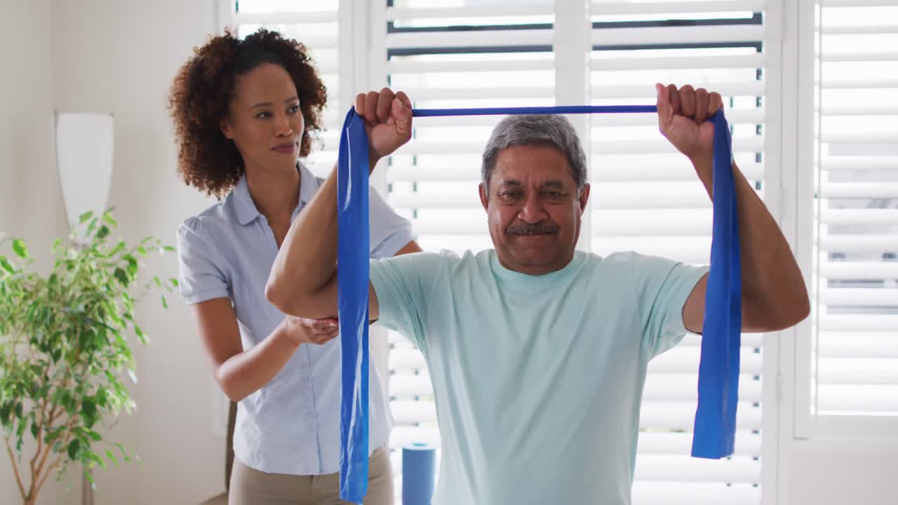 Fisioterapeuta mestiça ajudando homem idoso a se exercitar usando faixa elástica de exercício.