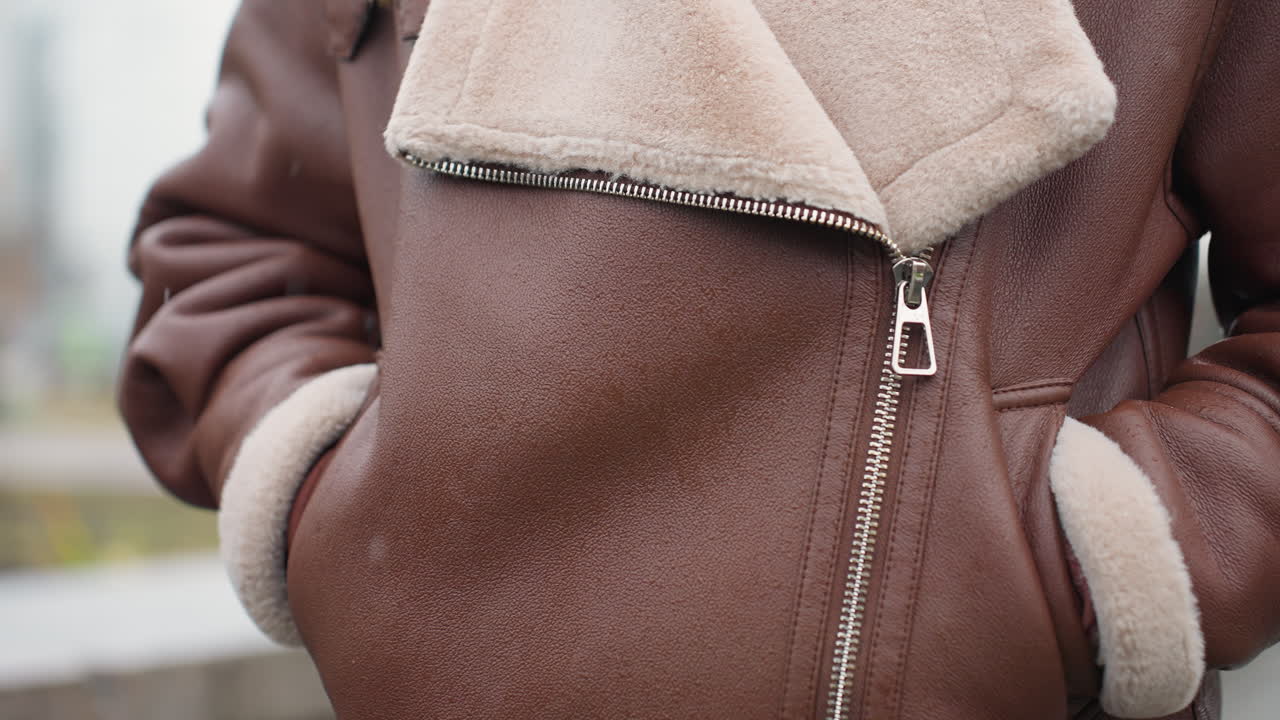Shot of someone's brown shearling jacket with hands tucked into pockets, face not visible, showcasing texture, warmth, and cozy appeal of winter outerwear on cold day with blurred outdoor background