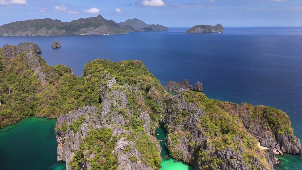 Aerial retreat from Big Lagoon on Miniloc Island, revealing dramatic limestone cliffs, vibrant blue waters, and lush tropical vegetation in the Bacuit Archipelago, northern Palawan