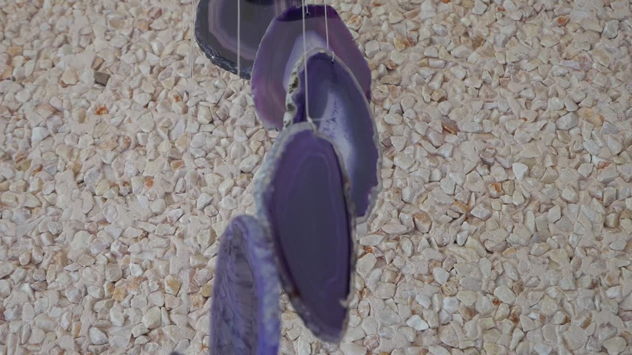 Close-up of purple agate gemstone wind chime hanging against textured stone wall in daylight