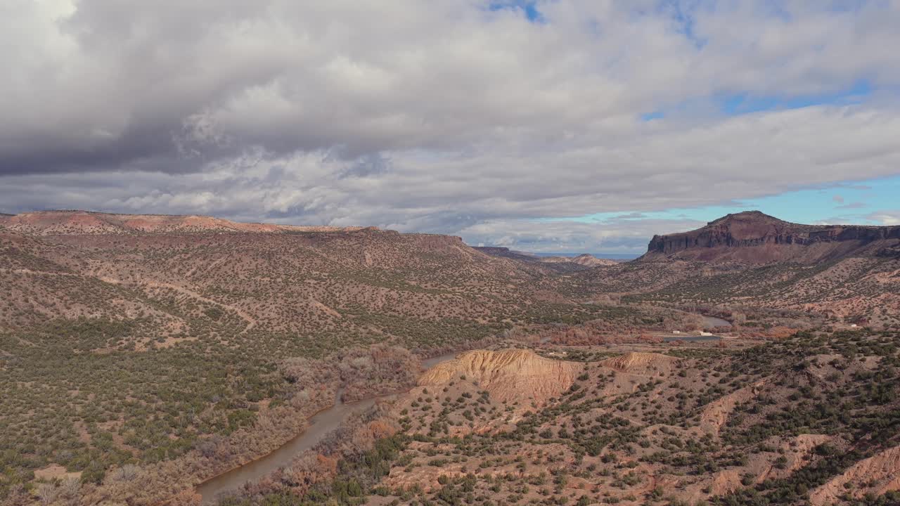 The drone continues its descent, revealing detailed canyon textures, winding river curves, and layered high-desert terrain below
