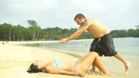 una mujer está tomando el sol acostada en la arena. un hombre está sosteniendo a una mujer con agua