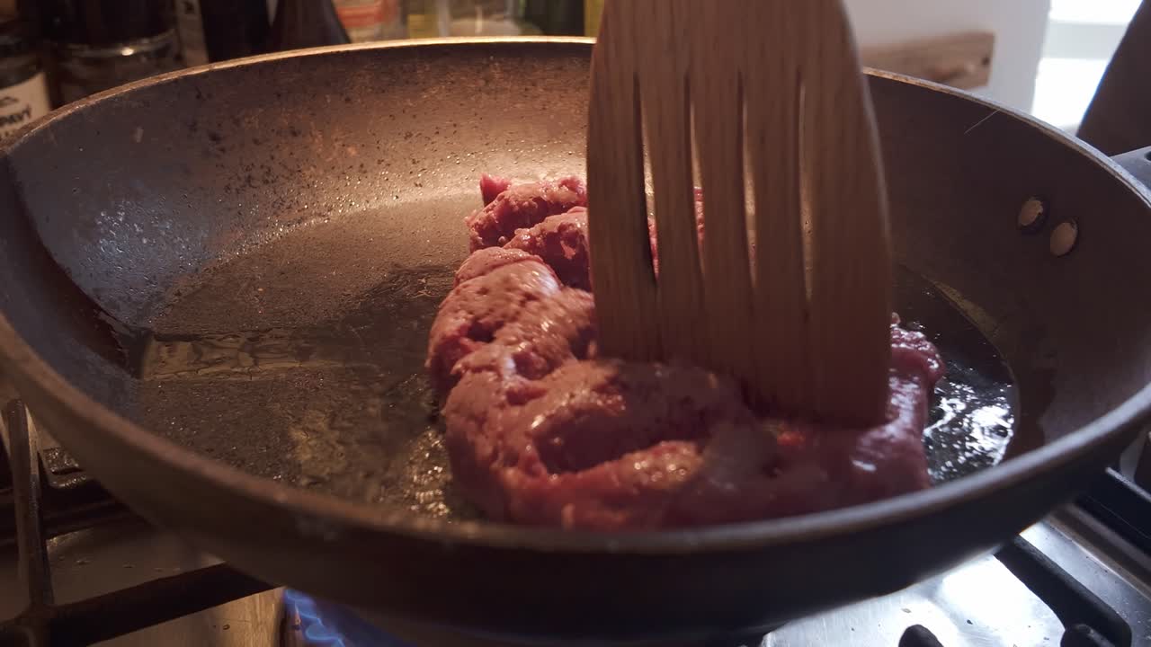 Home cook using spatula to spread mince beef in hot frying pan CLOSE-UP
