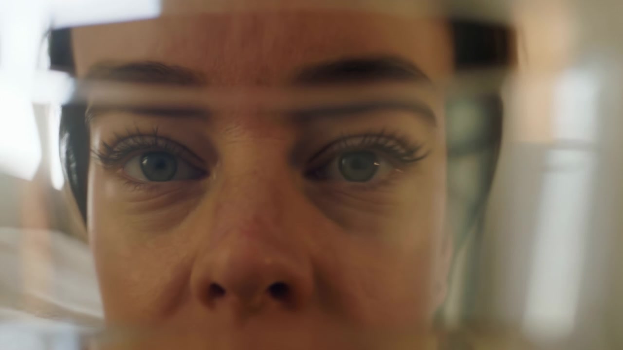 Gros plan d'un visage féminin vu à travers une vitre réfléchissante en intérieur, avec un œil nettement visible, un flou doux à l'avant-plan et à l'arrière-plan, une lumière beige chaude, une faible profondeur de champ et un cadrage abstrait en couches.