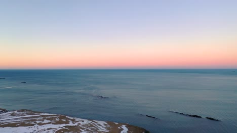 Panorámica-Aérea-Desde-Una-Llanura-Invernal-Vacía-Hasta-El-Mar,-Hermoso-Horizonte-De-Puesta-De-Sol