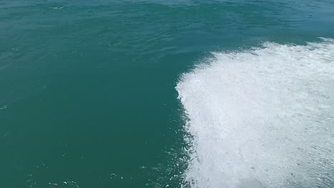Mass-of-water-displaced-from-a-small-boat-at-speed,-in-calm-and-blue-sea,-beautiful-effect-that-water-makes