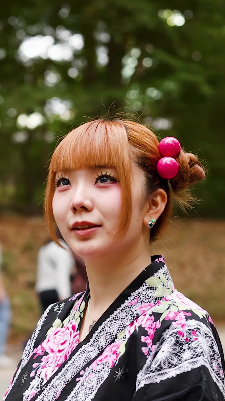 Giovane donna che indossa un yukata tradizionale con perline rosa nei capelli si trova in un parco di Tokyo.