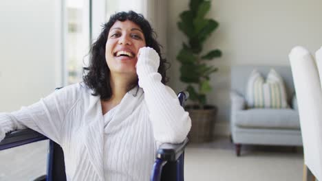 retrato de una feliz mujer discapacitada biracial en silla de ruedas riendo en la sala de estar