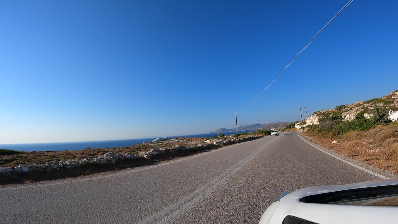 Point of view: A white car drives on a two-lane Greek road, summer vacation, view of the Mediterranean Sea