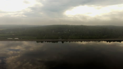 Aerial-footage-of-a-small-town-in-Finland,-approaching-from-a-calm-and-spooku-lake-by-dawn