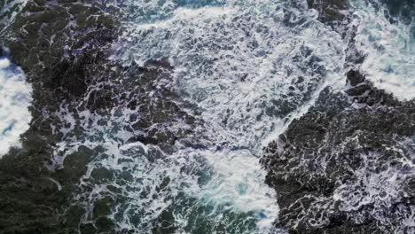 Top-down-aerial-view-large-ocean-waves-crashing-on-rocks-on-coast