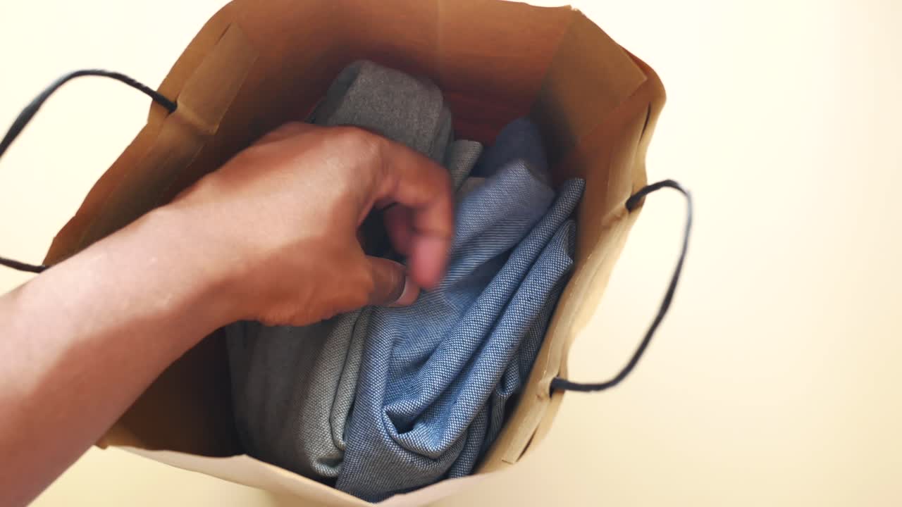 Hand holding clothes in a paper bag
