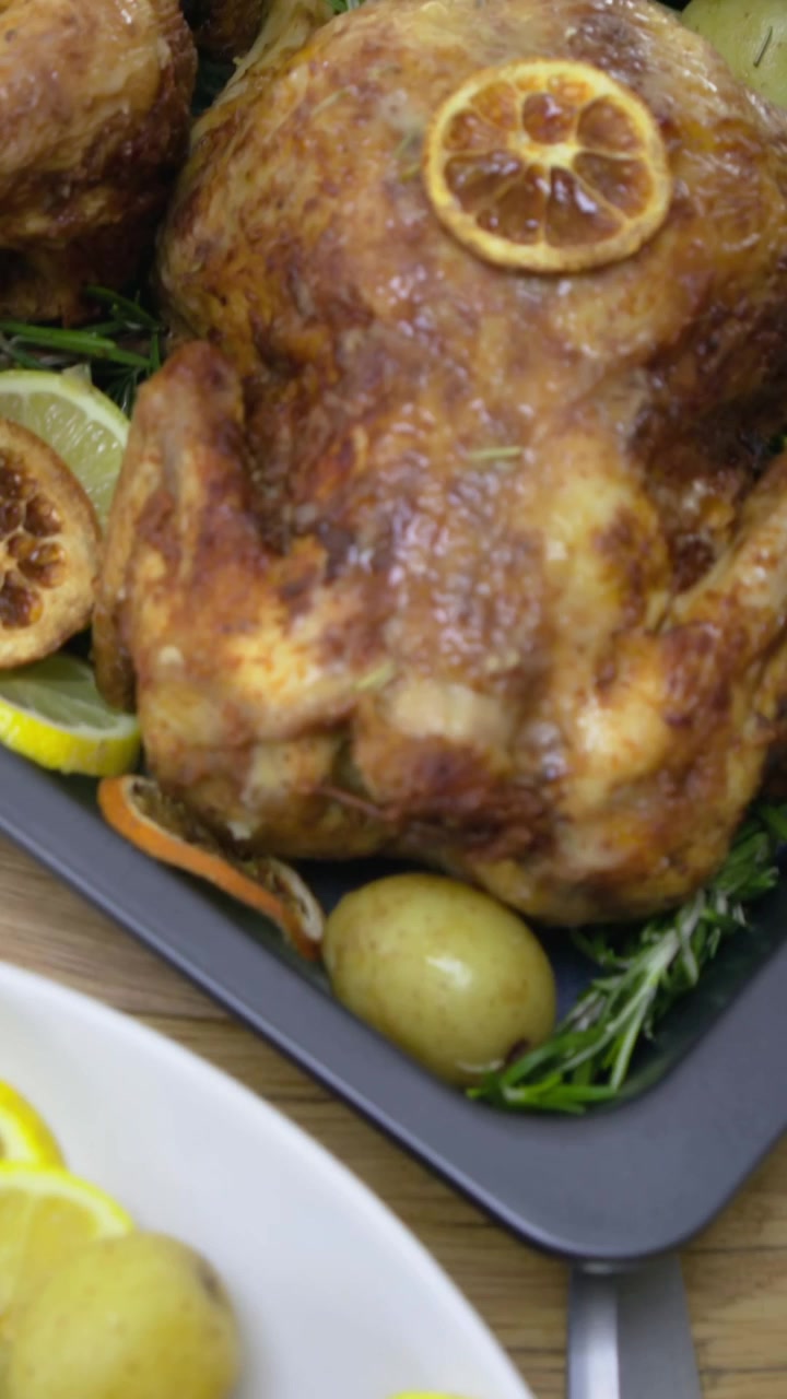 Video verticale: Telecamera scorrevole che rivela pollo arrosto su un tavolo con fette di limone, patate e baguette
