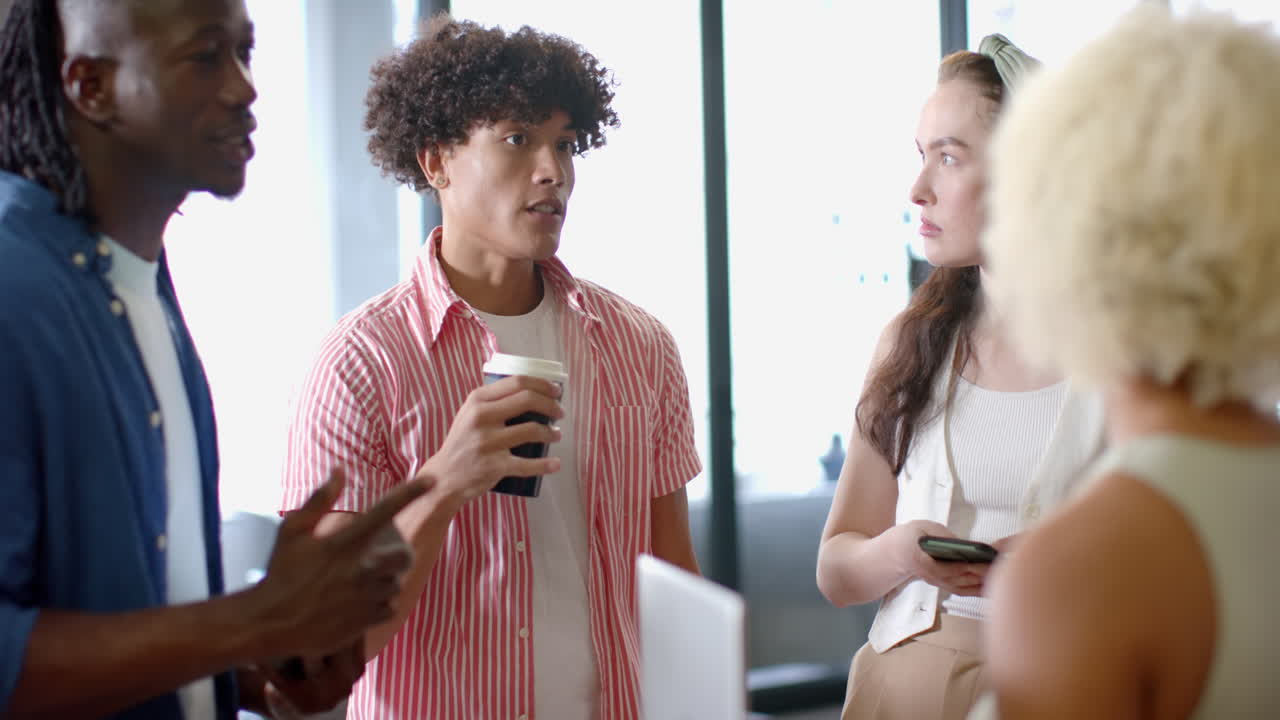 Discussing work, diverse colleagues holding coffee and smartphone in office meeting