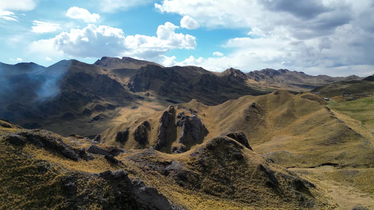 Aerial footage flying through the Andean mountains of Peru. A brush fire sends gentle smoke through golden valleys under late-afternoon sun