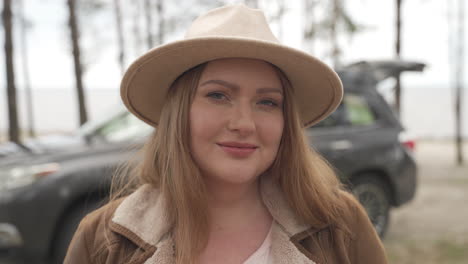 Portrait-Of-A-Beautiful-Red-Haired-Woman-Wearing-A-Camel-Hat-In-Front-Of-A-Car-In-The-Countryside