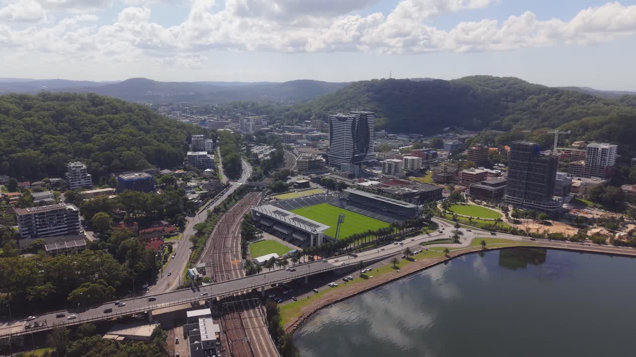 Drone establishing descending full stadium showing seating symmetry, grass field, nearby roads and infrastructure, Central Coast NSW Australia