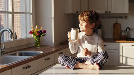 young boy in pajamas enjoying a drink on a sunny morning in the kitchen