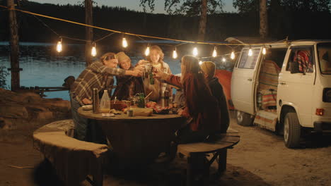 amigos jóvenes haciendo sonar bebidas en tostadas en la cena de campamento