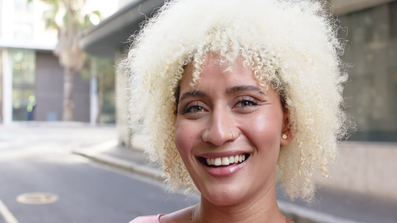 Young biracial woman with curly blonde hair smiles brightly in the city