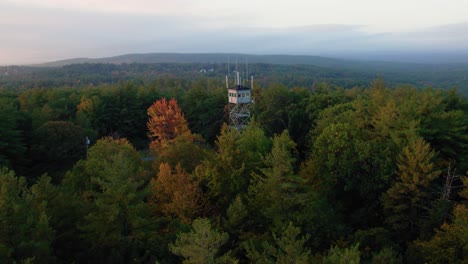 aerial drone of fire tower above autumn trees and orange fall leaves at sunrise