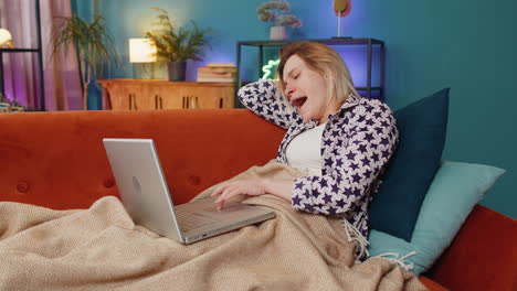 bored sleepy young caucasian woman working on laptop computer falling asleep at home couch