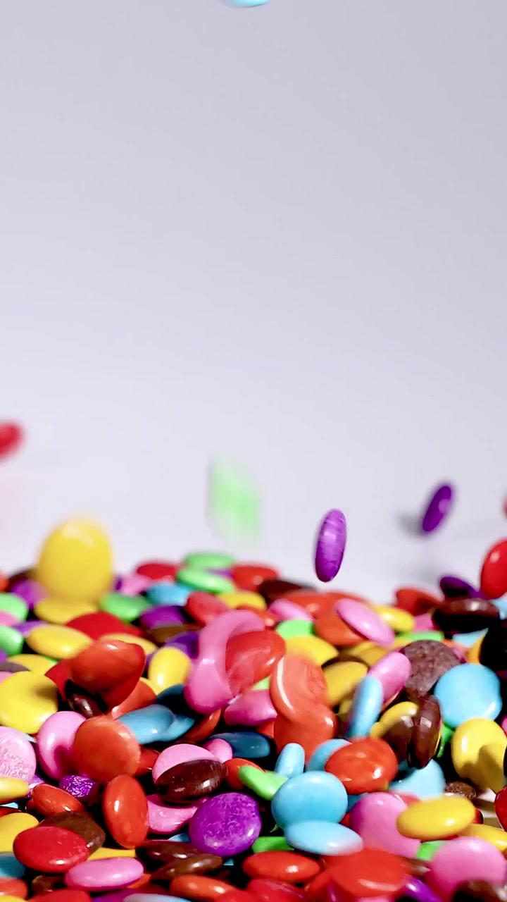 Una toma vertical de chocolates de colores recubiertos de caramelo cayendo en cascada sobre una pila creciente contra un fondo blanco