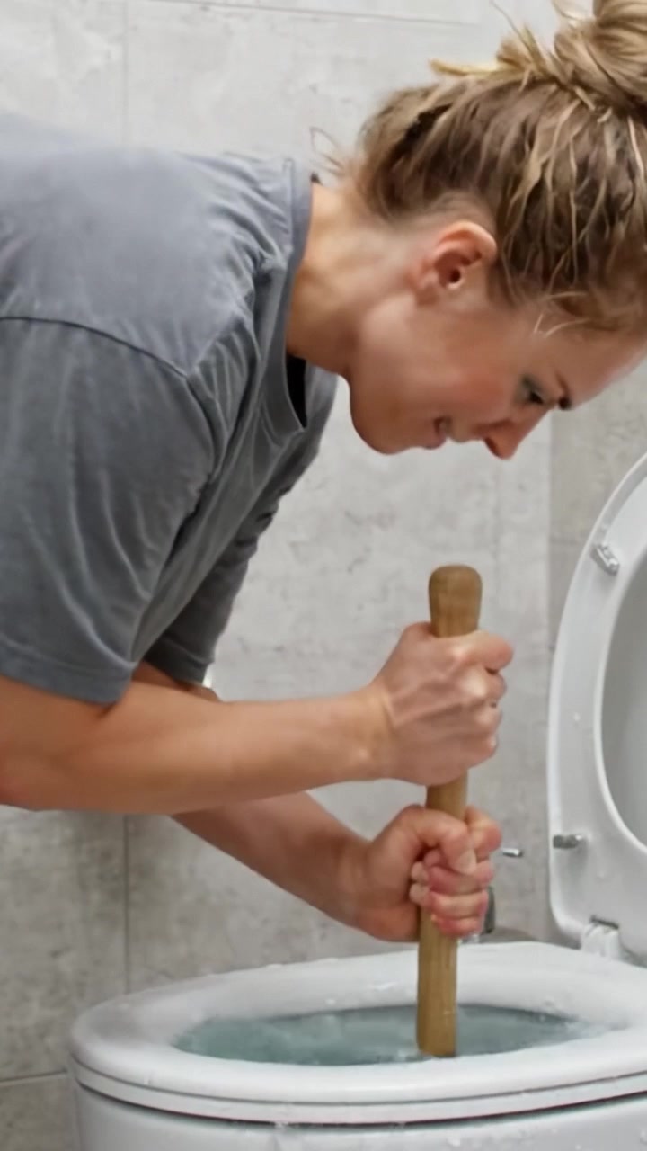 Donna che stura con decisione il gabinetto usando uno sturalavandini, dimostrando un'efficace tecnica di manutenzione domestica e capacità di risoluzione dei problemi in un ambiente bagno.