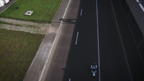 Drone-shot-of-a-front-facing-motorcycle-passing-throw-below-in-a-rather-industrial-area-at-sunset