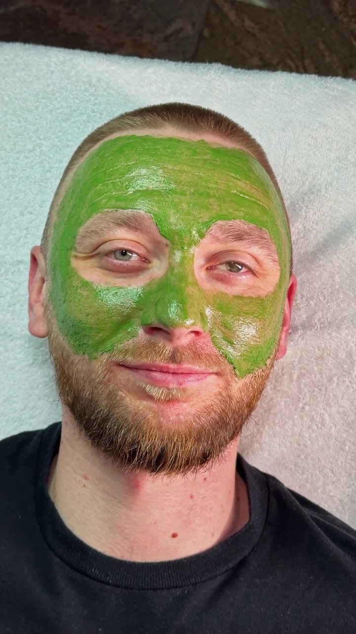 Homem recebendo um tratamento de máscara de argila verde num centro de bem-estar para cuidados com a pele à tarde