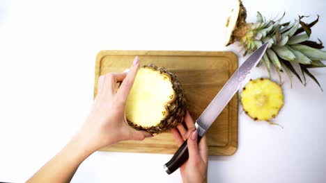 Tropical fruit on a board. Female's hands cleaning fresh pineapple with a knife on a cutting board. Top view.