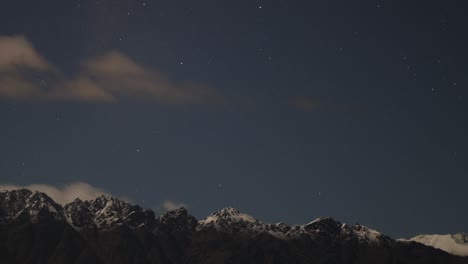 A serene night sky with stars and clouds over snow-capped mountains in Queenstown, New Zealand. Captured with steady camera and soft lighting