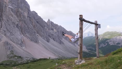 blonde tourist girl on a swing in the mountains in the italian alps, alleghe, dolomite near refugio tissi, italy