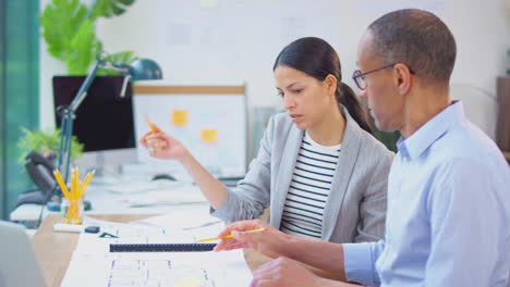 male and female architects working in office together at desk on plans for new building