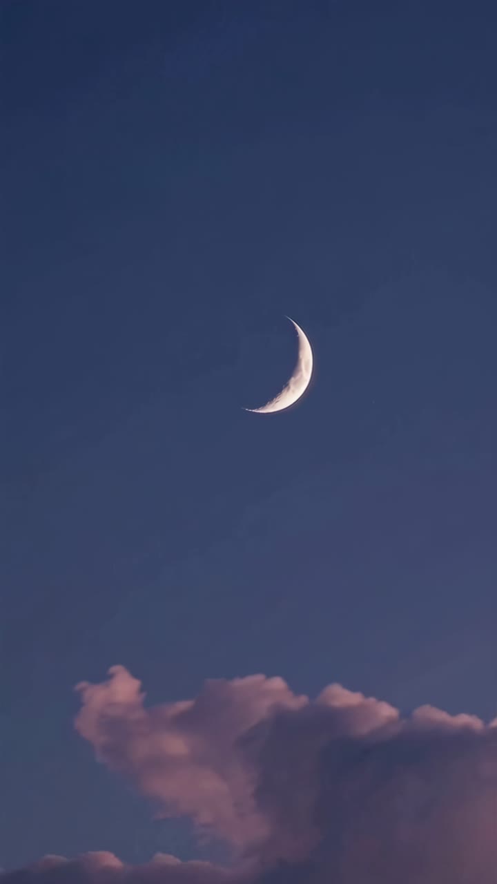 A serene crescent moon in a twilight sky with pink clouds, captured from a low angle