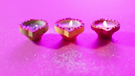 Close-up-of-burning-colourful-candles-celebrating-diwali-on-purple-background