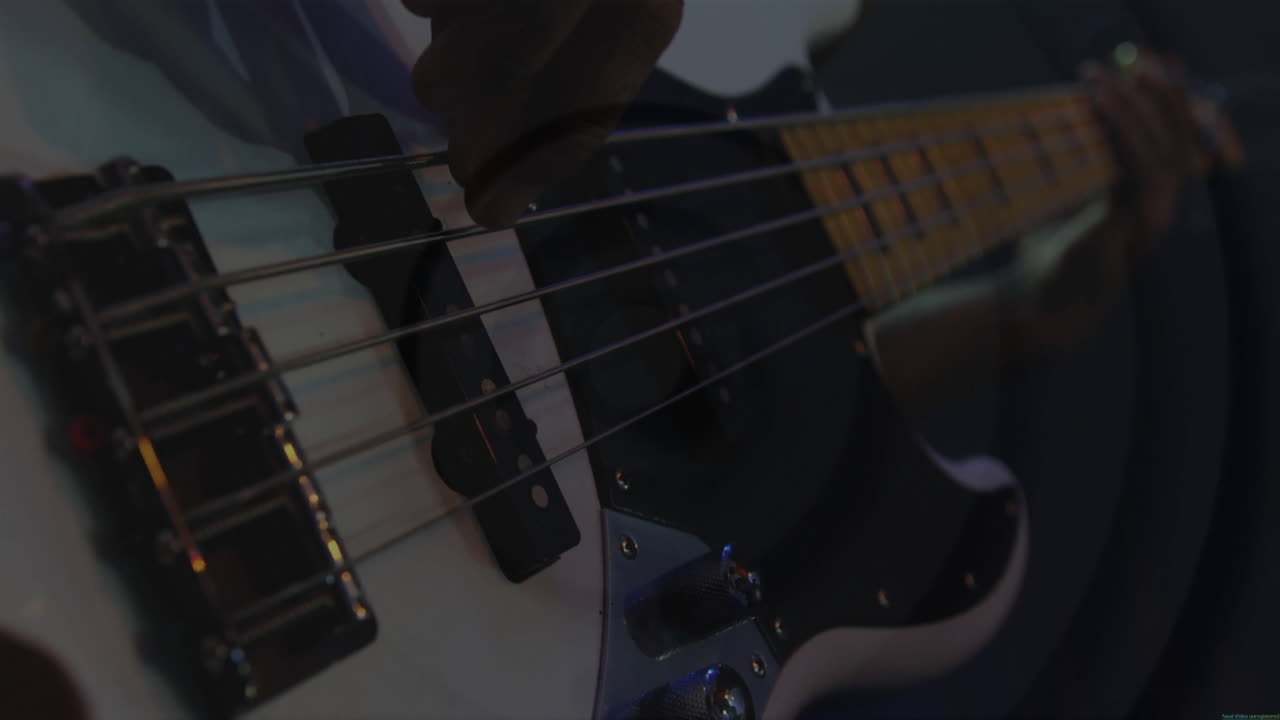 Musician plucking bass guitar strings in dim music studio, displaying animated waveform graphics