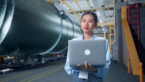 an asian business woman using laptop computer an looking around in pipe manufacturing factory