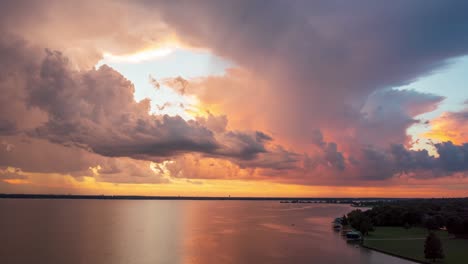 aerial hyper lapse above coastal region as sunset golden hour light illuminates pillars of cloudy sky