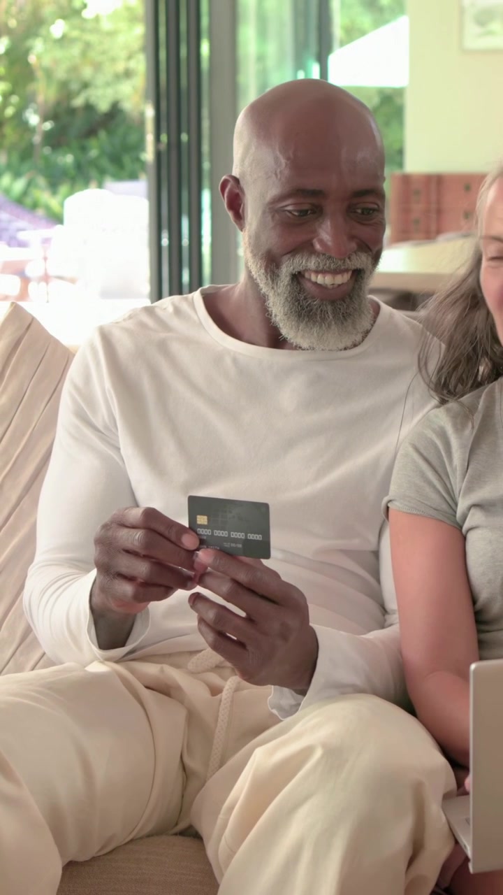 Vertical video: Finding card, adult man checking it on sofa by doors, woman on laptop hugging him
