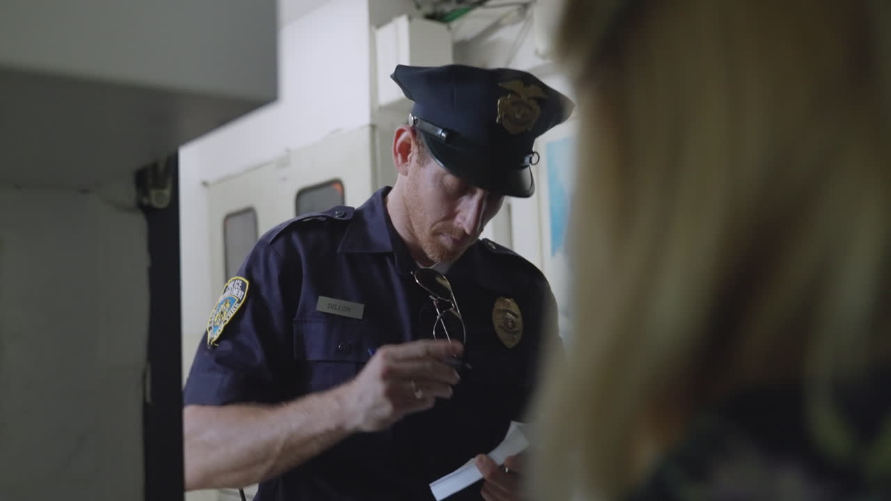 Police officer, investigator, or detective stands at a woman's front door, questioning her and writing notes in a small notebook. Witness statement, investigation, law enforcement, crime-solving, Cop.